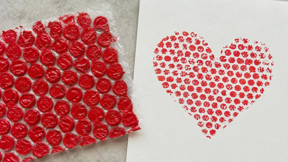 Red-painted bubble wrap beside a paper heart print of tiny dots.