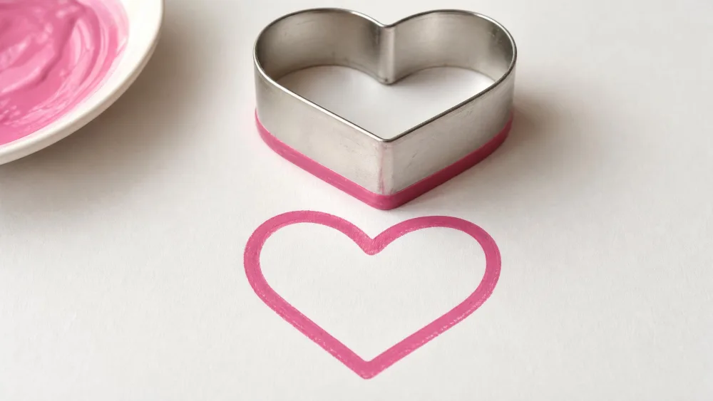 Heart cookie cutter dipped rim-down in pink paint, stamping an outline.