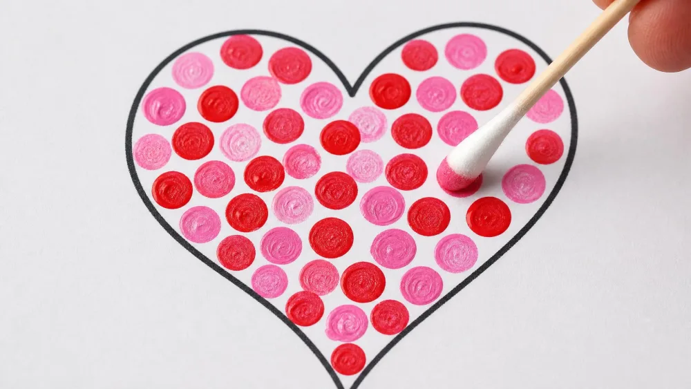 Cotton swab dotting red and pink paint inside a heart outline.