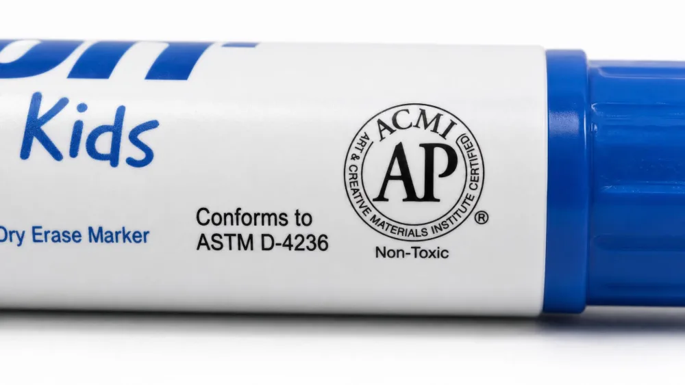 Close-up of a kids' dry erase marker barrel showing the printed "Conforms to ASTM D-4236" safety line and the round ACMI AP non-toxic seal.