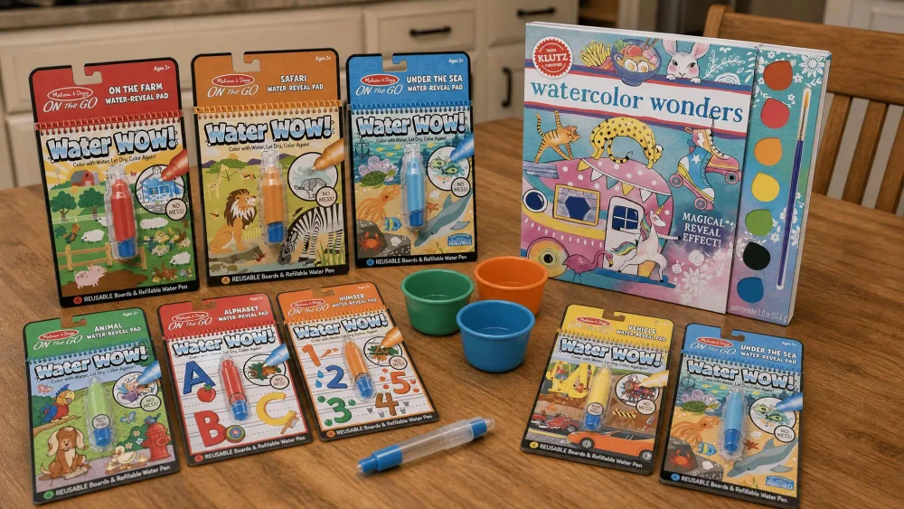 Several kids' watercolor books and water cups arranged on a kitchen table for testing