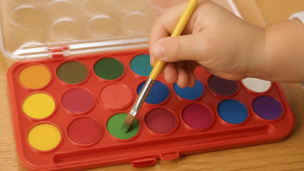 A toddler's hand loading a brush from an oversized pan in the Melissa & Doug Deluxe set.
