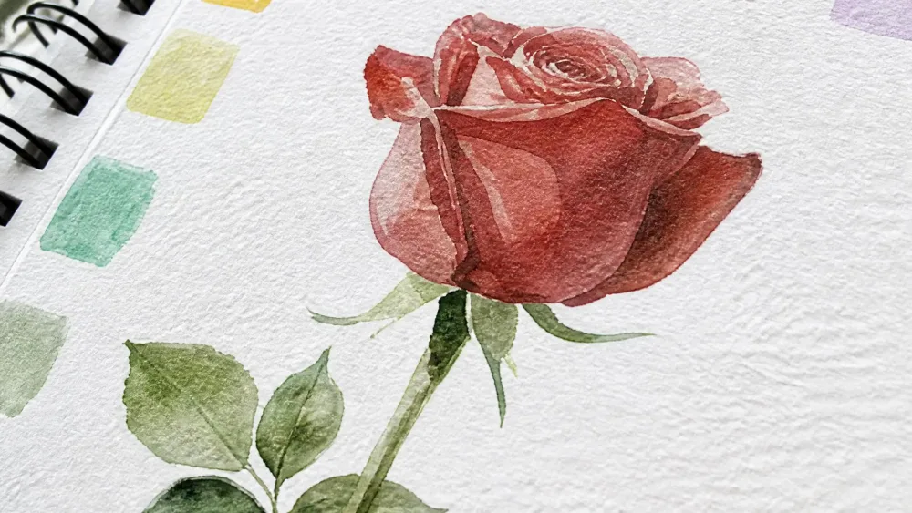 A close-up of a painted flower design on KOROI Watercolor Workbook's thick 300gsm cotton cold-pressed paper, showing visible paper texture and pooled watercolor pigment.