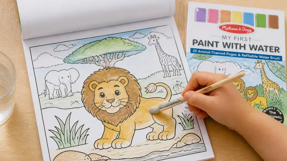 A child's hand holding the included brush over an open Melissa & Doug My First Paint with Water Animals pad, with a lion outline turning color as water is brushed across the page.