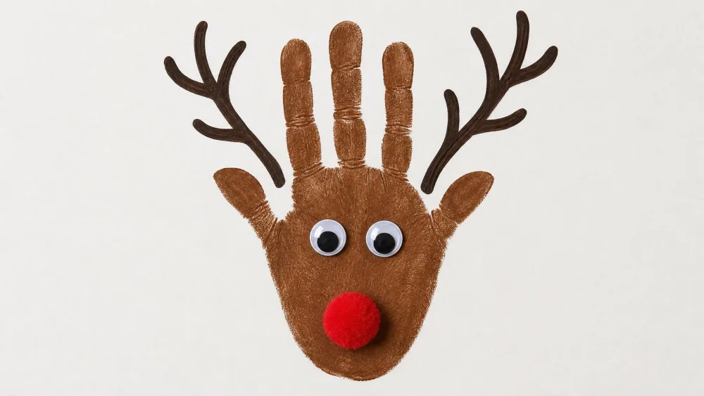 A brown handprint turned into a reindeer with googly eyes, a red pom-pom nose, and antlers.