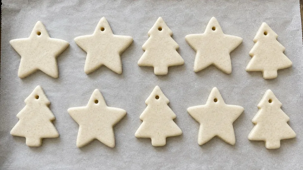 Salt dough cut into star and tree ornaments on parchment, each with a hole poked for ribbon.