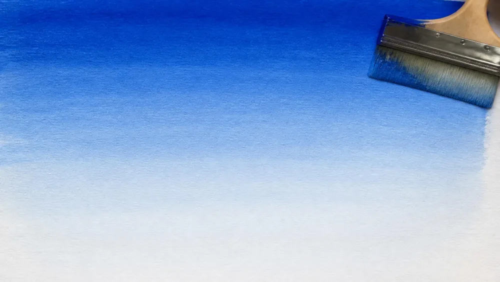 A wide brush sweeping a graded blue wash across paper, deep at the top and fading to pale near the bottom, like a sky.