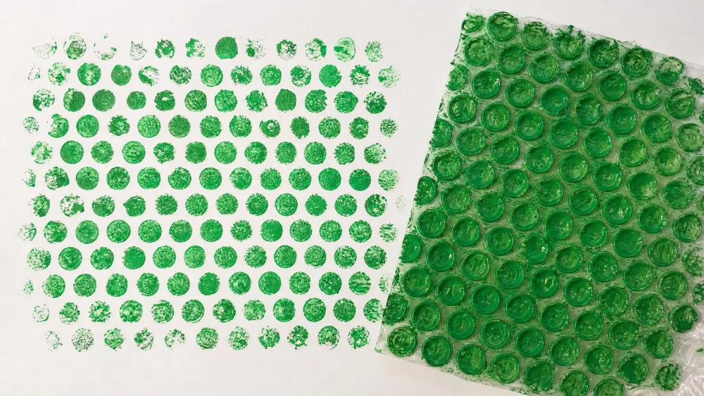 A sheet of bubble wrap coated in green paint pressed onto paper, revealing a dotted print.