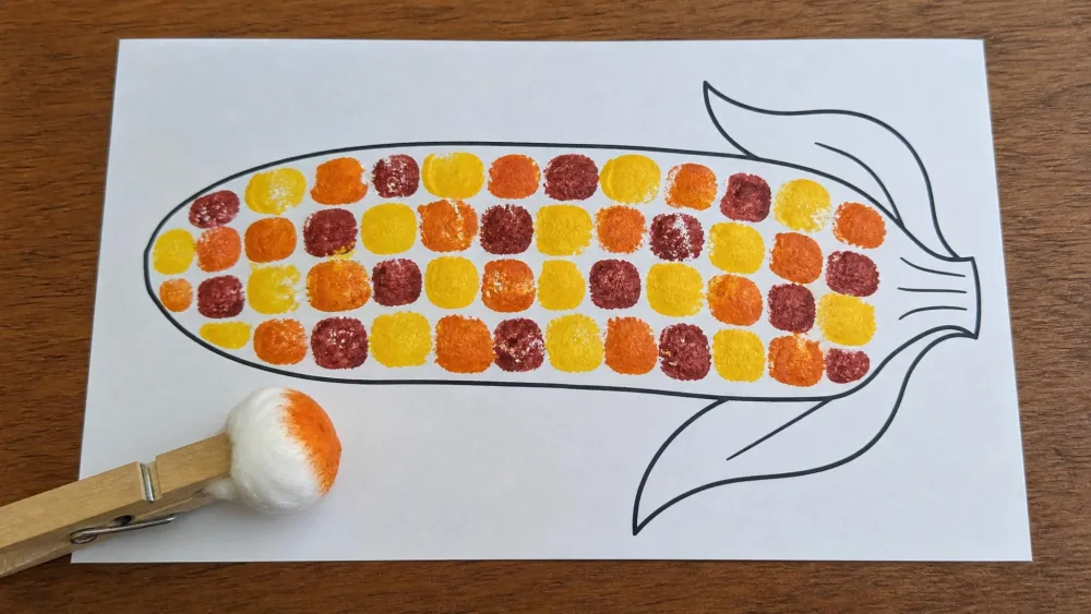 Fall-colored kernels stamped onto a corn cob outline with a cotton ball in a clothespin.