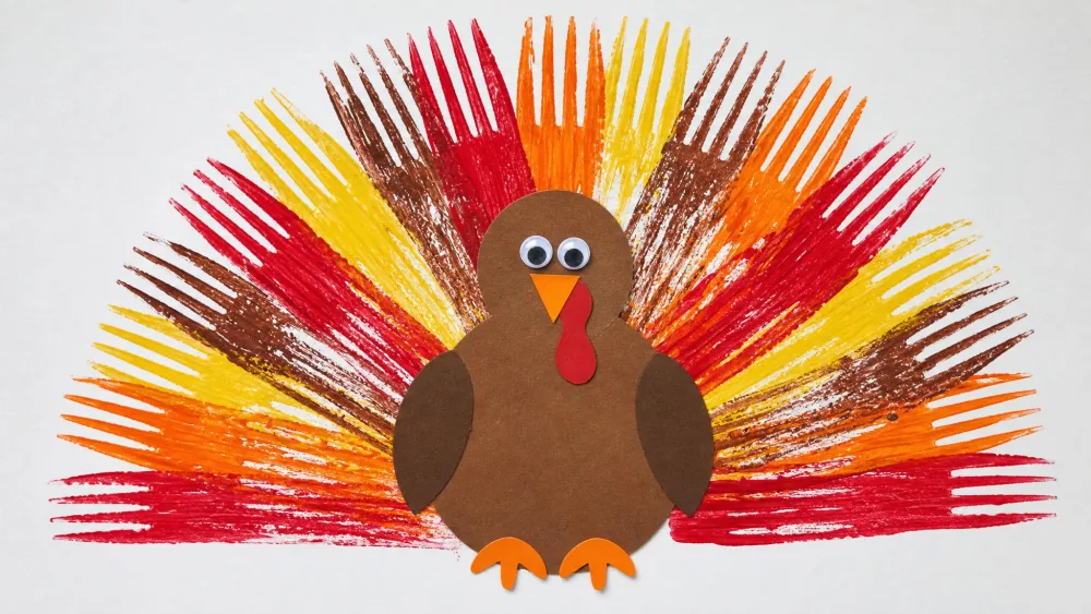 Fanned feather prints made by pressing a paint-dipped fork onto paper behind a turkey.
