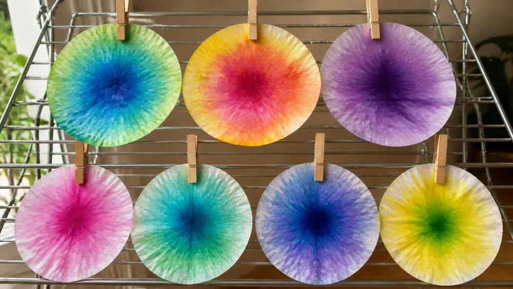 Round coffee filters colored with liquid watercolor, clipped to a drying rack with the dye blooming and blending toward the center of each filter.