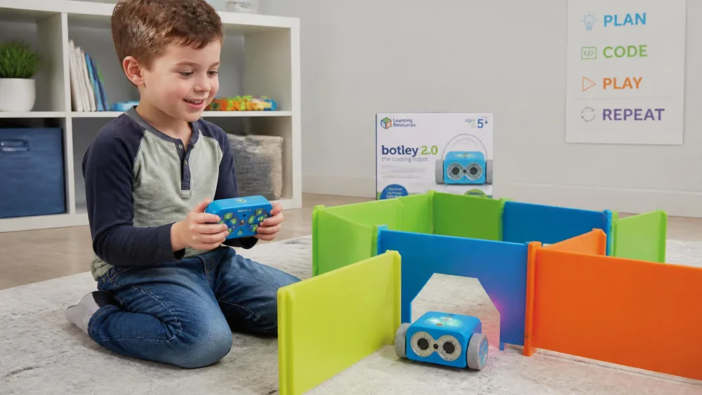 A six-year-old holding the Botley 2.0 remote as the blue robot rolls through coloured walls.