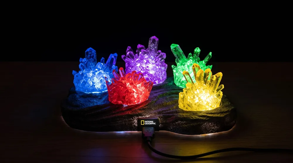Five grown crystals in blue, red, purple, green and yellow on the illuminated USB display from the National Geographic Mega Crystal Growing Kit, in a darkened room.