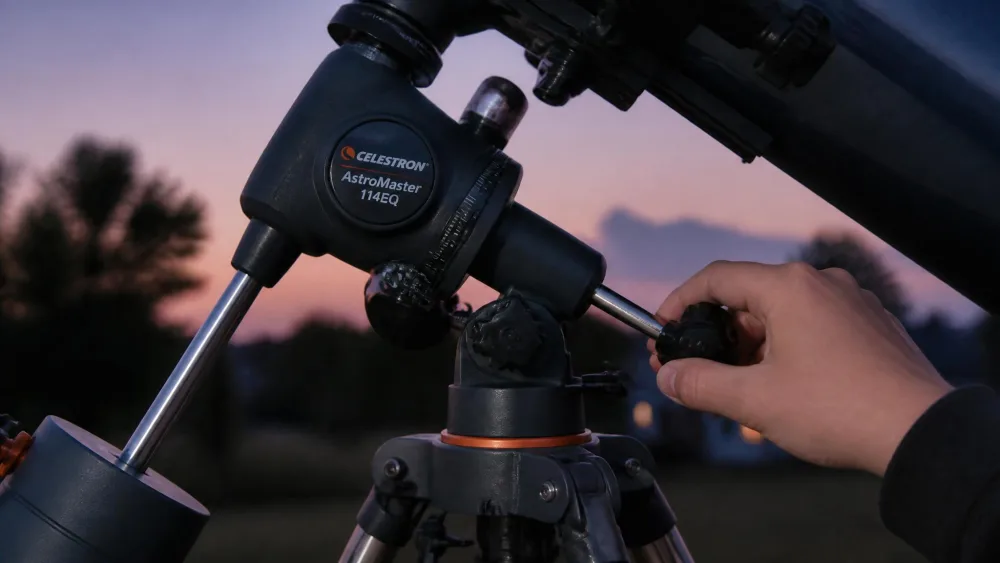 Close-up of the German equatorial mount on a Celestron AstroMaster 114EQ, with a teenager's hand turning one of the slow-motion control knobs at dusk.