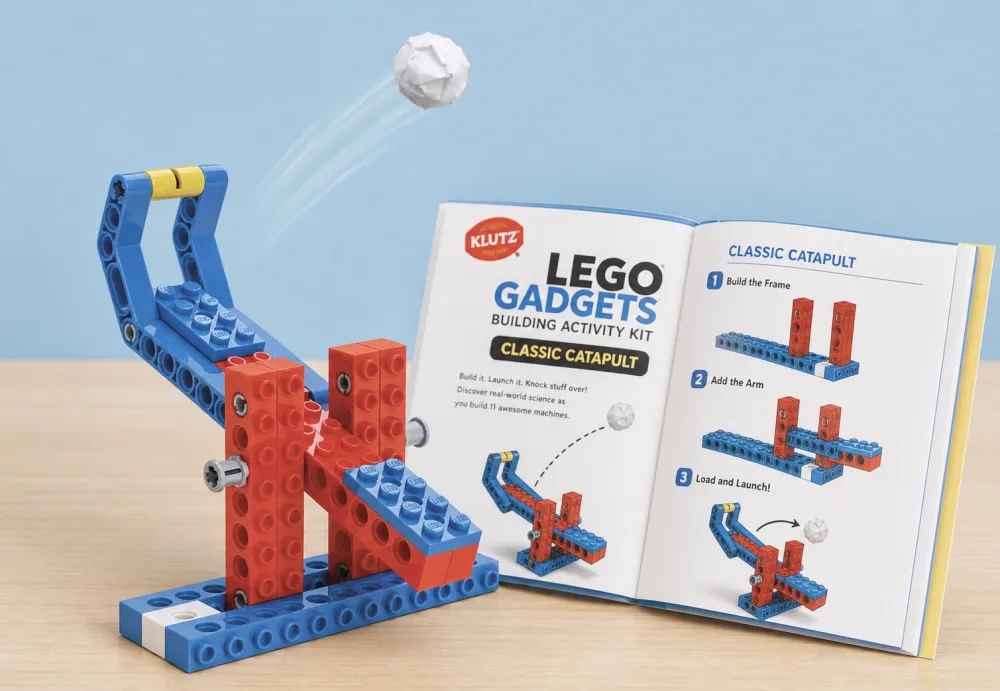 The Klutz LEGO Gadgets Classic Catapult launching a small paper ball into the air, with the open instruction book beside it.