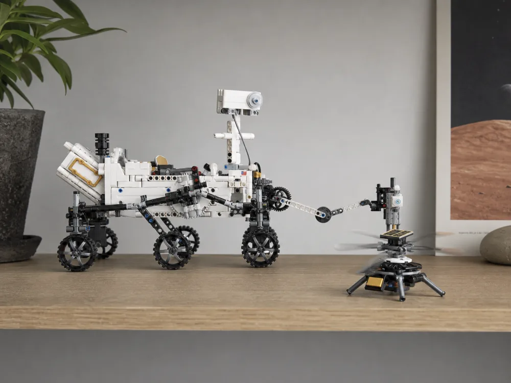The completed LEGO Technic 42158 Ingenuity helicopter model with spinning rotors sitting beside the white Mars rover on a shelf, showing the sticker-applied golden sections.