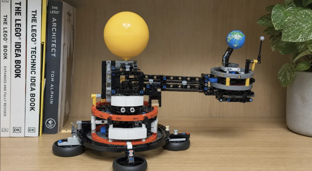 The assembled LEGO Technic 42179 orrery on a bookshelf, showing the printed Earth globe on its bulky support arm with the Moon and Sun arms and the month ring around the base.