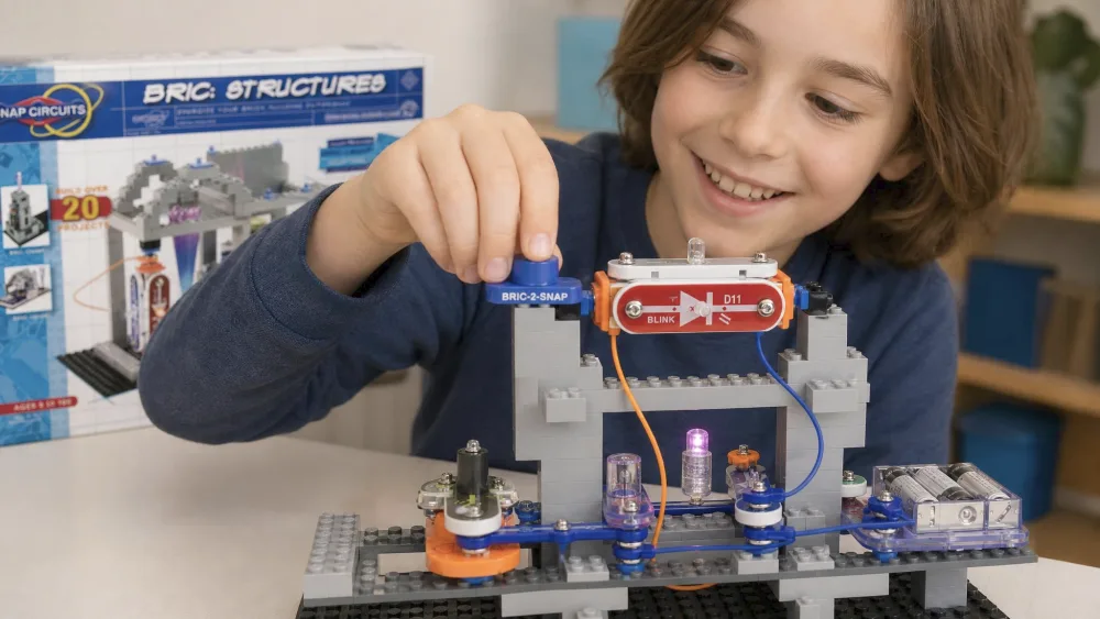 A child snapping a Bric-2-Snap adapter onto a brick tower built from Snap Circuits BRIC pieces, with a small LED glowing inside the structure.