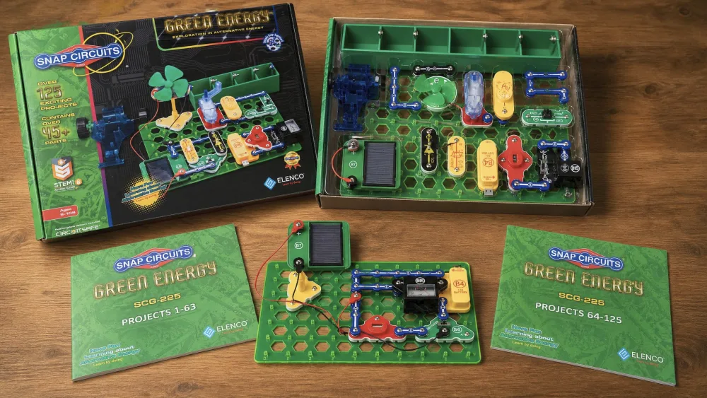 The open Snap Circuits Green Energy SCG-225 box with color-coded snap-together parts, the solar cell, and both manuals on a wooden table.