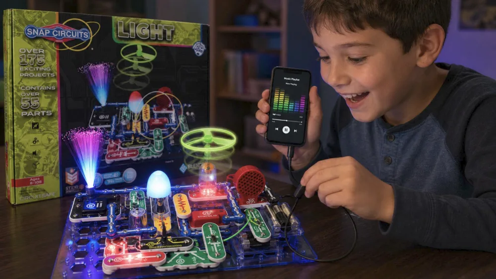 Child connecting a phone to the Snap Circuits LIGHT color-organ circuit, LEDs flashing to music.