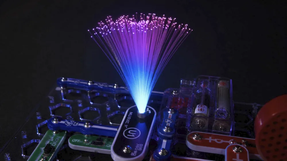 Close-up of the Snap Circuits LIGHT fiber-optic cable glowing at its tip in a dim room.